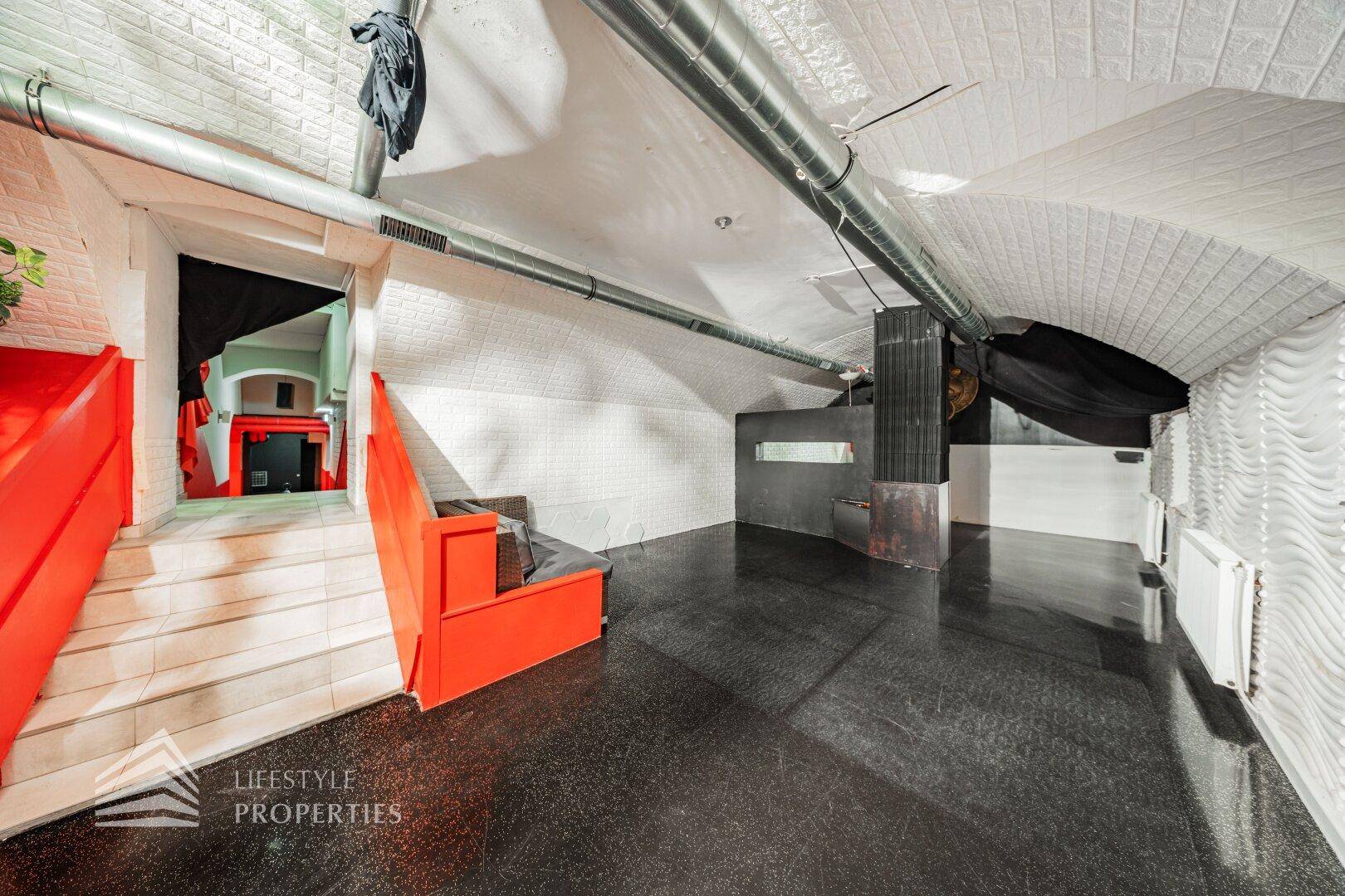 Großer Lounge-Bereich mit gewölbter Decke, freiliegenden Rohren und moderner, dunkler Bodenfläche.