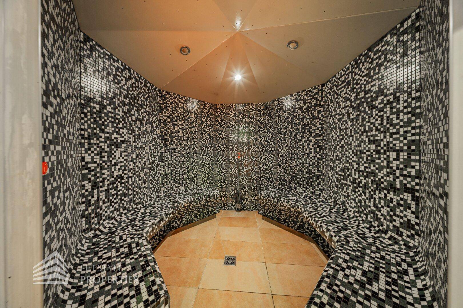 Dampfbad mit schwarzen und weißen Mosaikfliesen, geschwungenen Bänken und indirekter Beleuchtung.