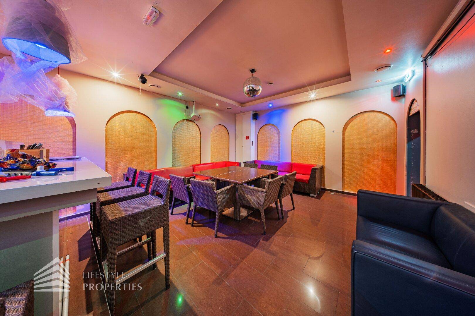 Geräumiger Bar-Lounge-Bereich mit Sitzgruppen, Discokugel und farbiger Beleuchtung für Unterhaltung.