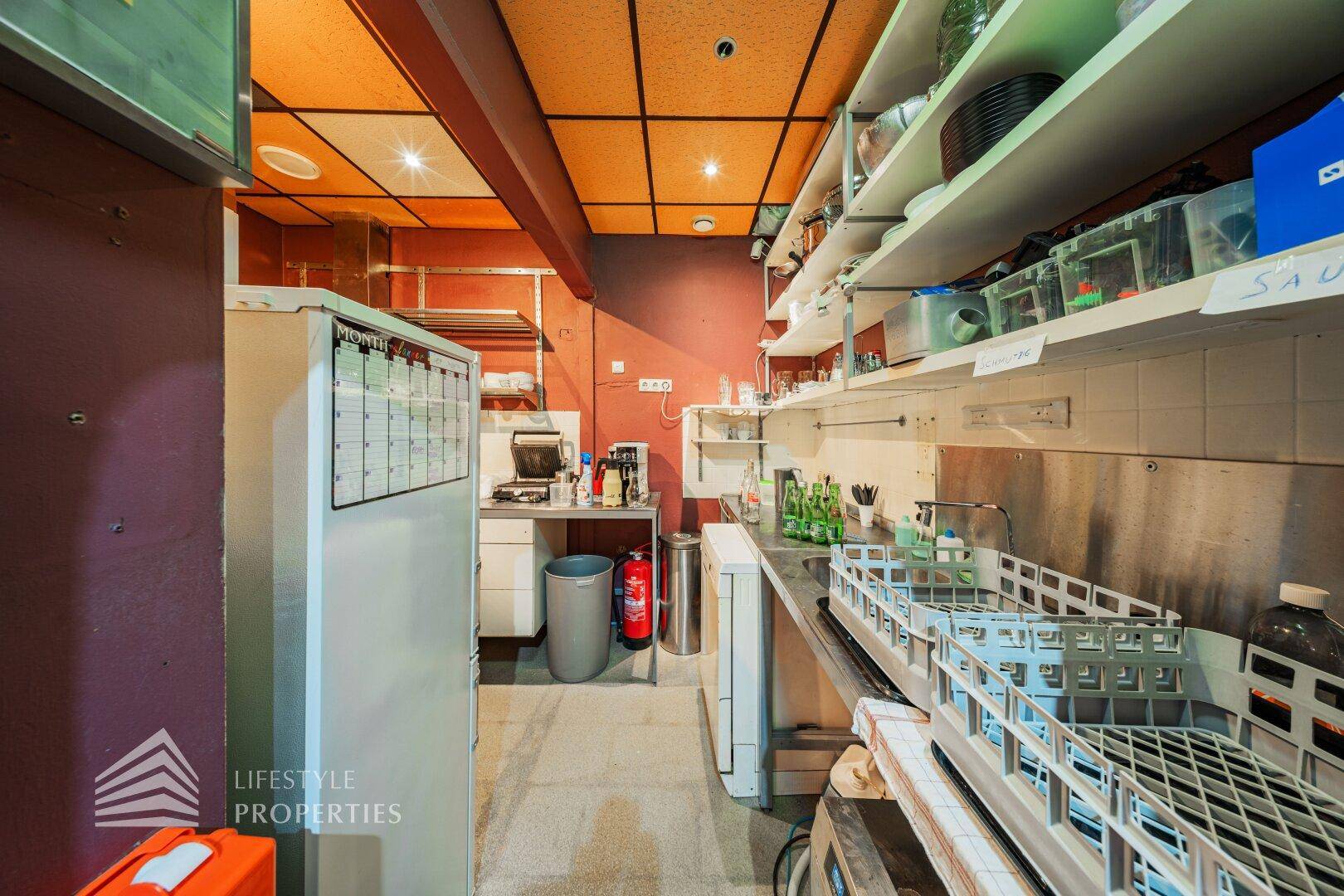 Industrielle Küche mit Edelstahlflächen, Regalen und Geräten, ideal für Catering oder Gastronomie.