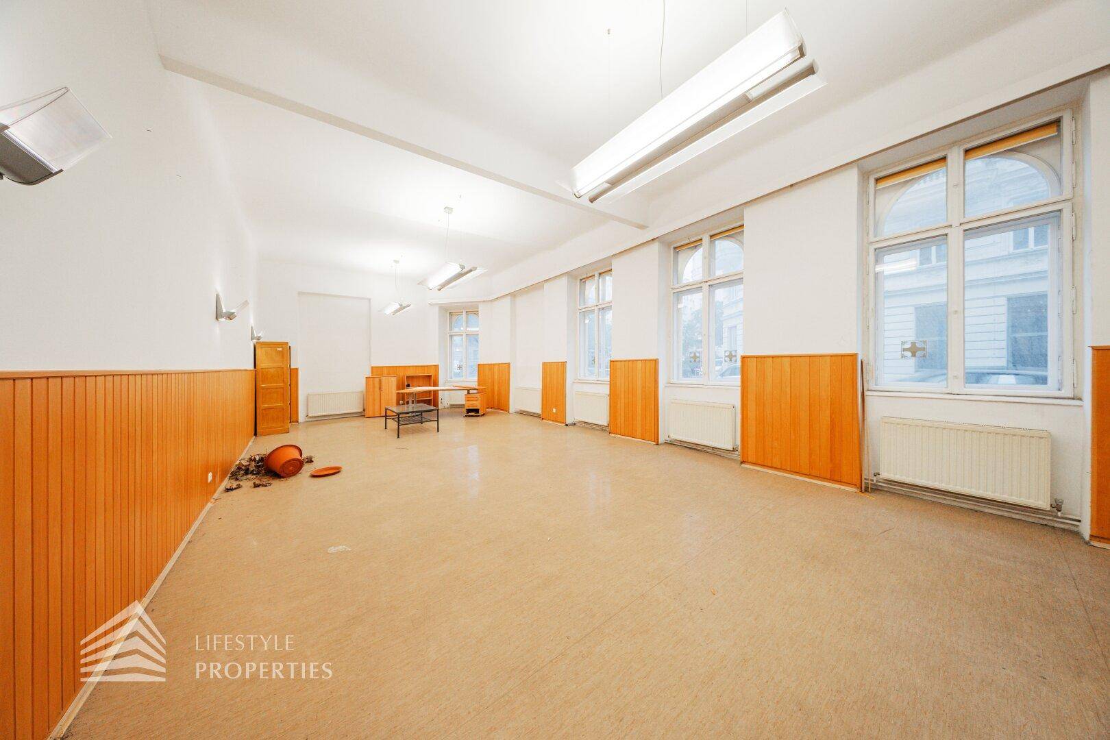 Geräumiger, heller Raum mit hohen Decken, Holzvertäfelung und großen Fenstern, bietet viel Tageslicht.