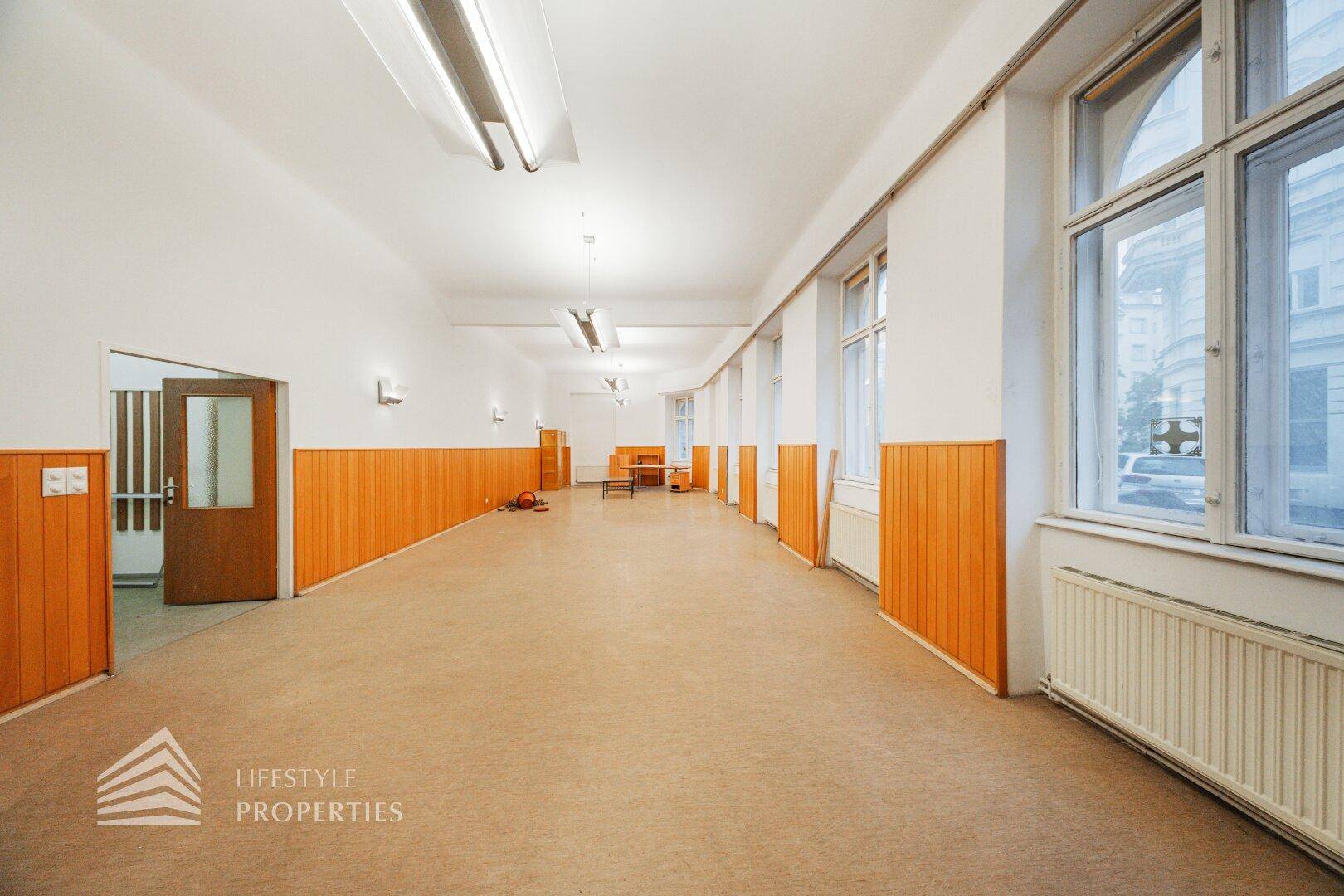 Langer, heller Raum mit Holzvertäfelung, hohen Fenstern und Zugang zu weiteren Bereichen, sehr gepflegt.
