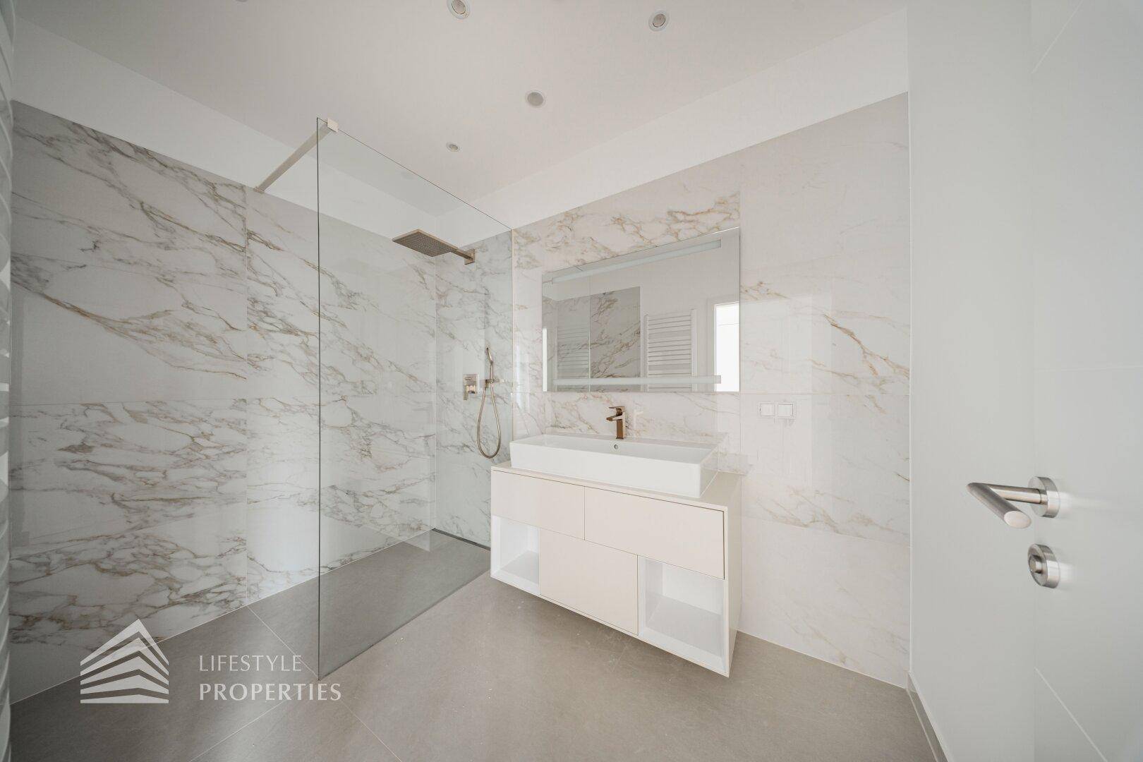 Luxuriöses Badezimmer mit großer begehbarer Dusche, Marmorfliesen und modernem Waschtisch.