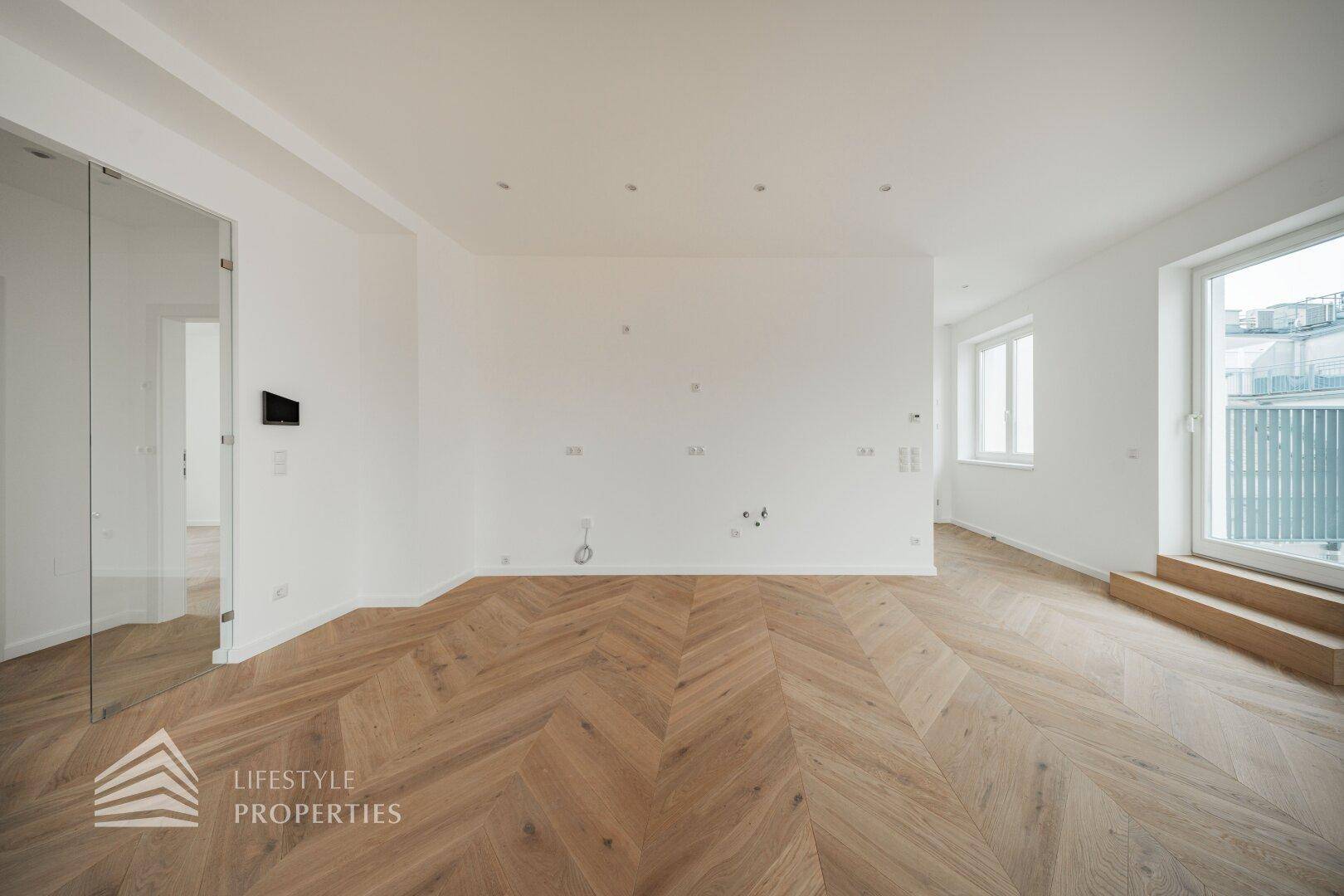 Modernes, leeres Zimmer mit Fischgrätparkett, Einbaustrahlern und Zugang zu einem Außenbereich.
