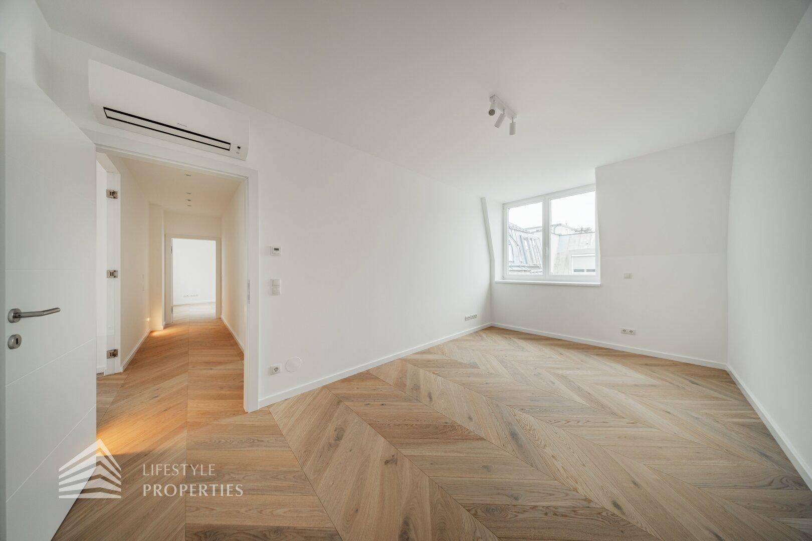Helles Zimmer mit Fischgrätparkett, Klimaanlage und einem Fenster mit Blick auf die Stadt.