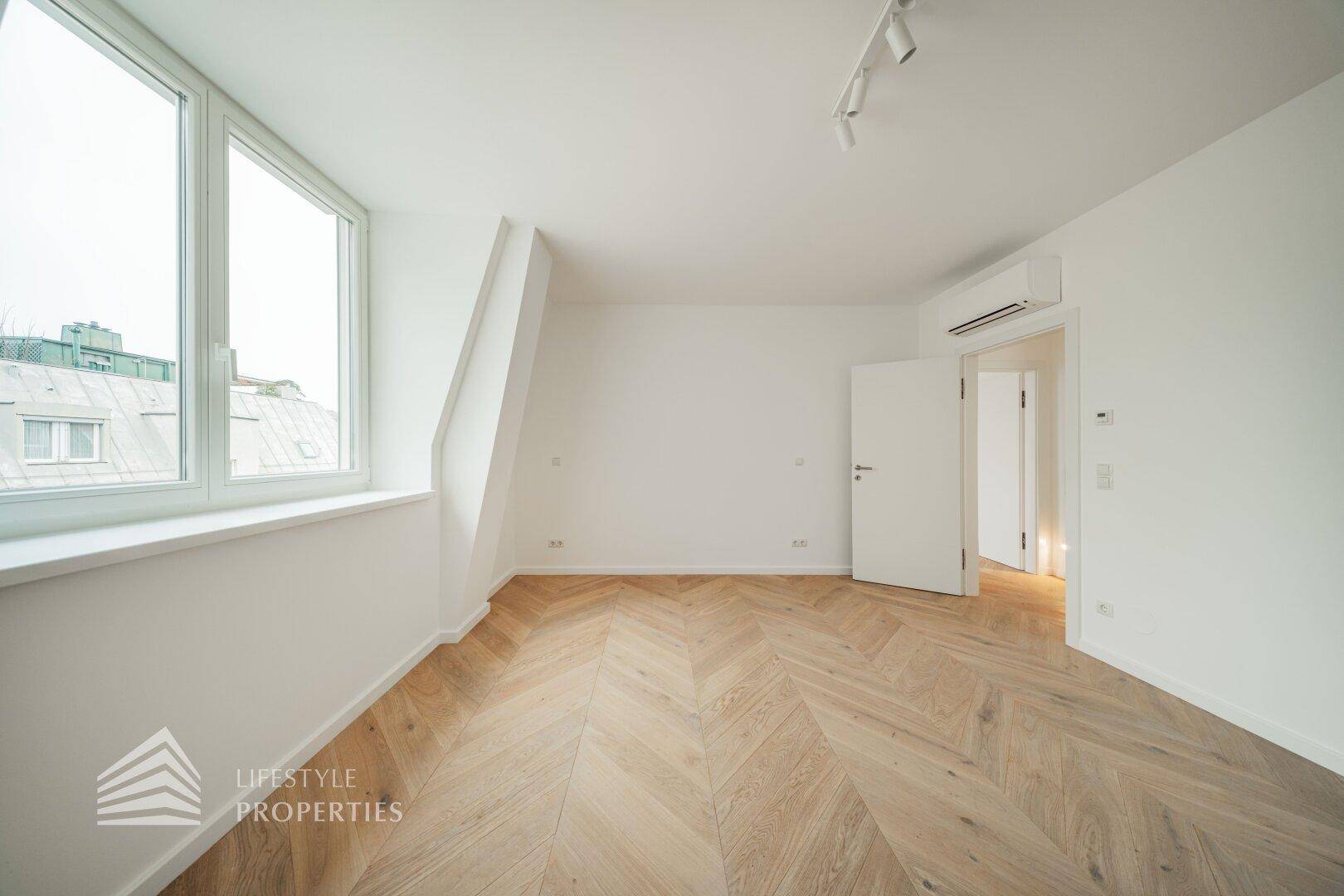 Helles Schlafzimmer mit Fischgrätparkett, Klimaanlage und einem Fenster mit Blick nach draußen.