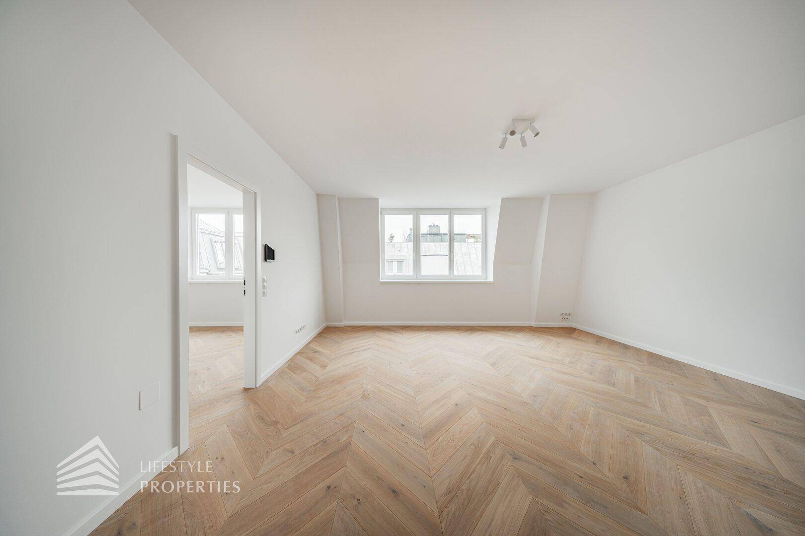 Geräumiges, helles Zimmer mit elegantem Fischgrätparkett und großen Fenstern.