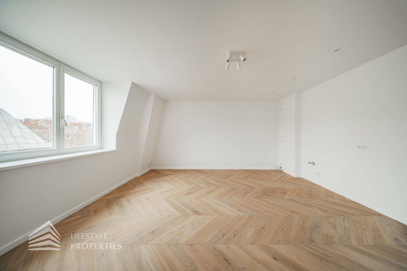 Großes, lichtdurchflutetes Zimmer mit Fischgrätparkett und weitem Ausblick.