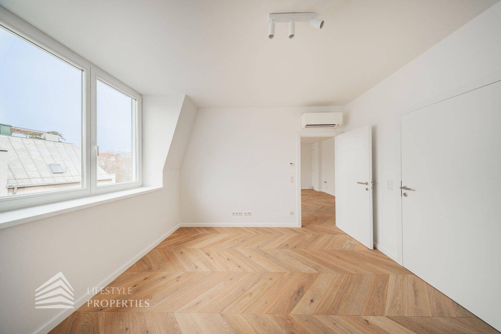 Modernes Zimmer mit Fischgrätparkett, weißen Türen und Klimaanlage.