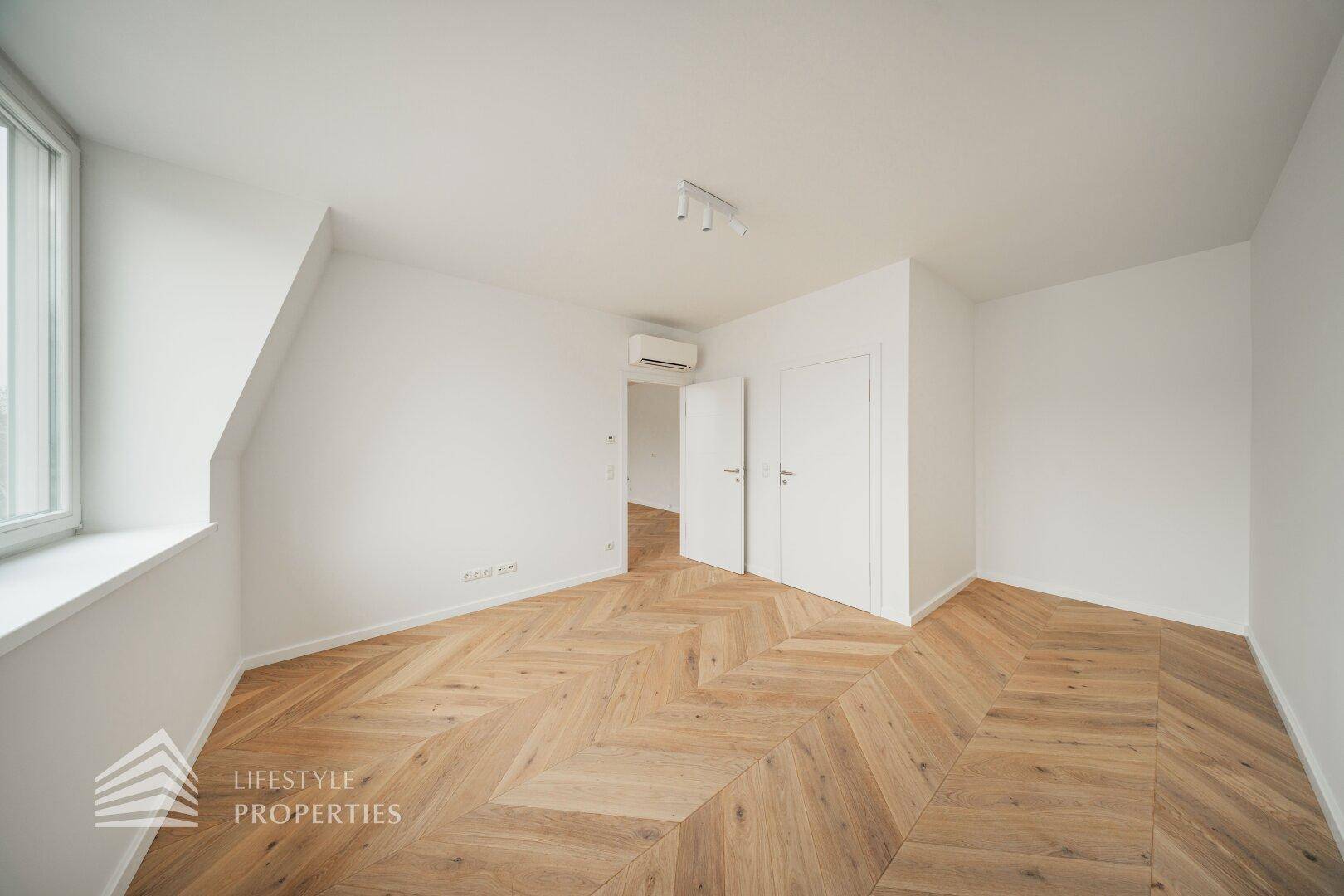 Helles Schlafzimmer mit Fischgrätparkett, weißen Wänden und integrierter Klimaanlage.