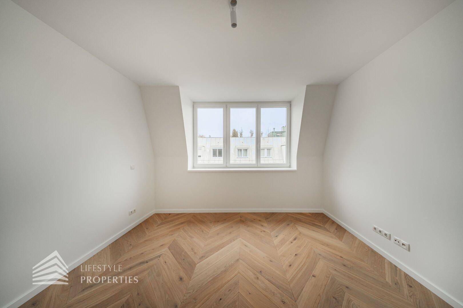 Ruhiges Zimmer mit Fischgrätparkett und einem Fenster mit Blick auf die Umgebung.
