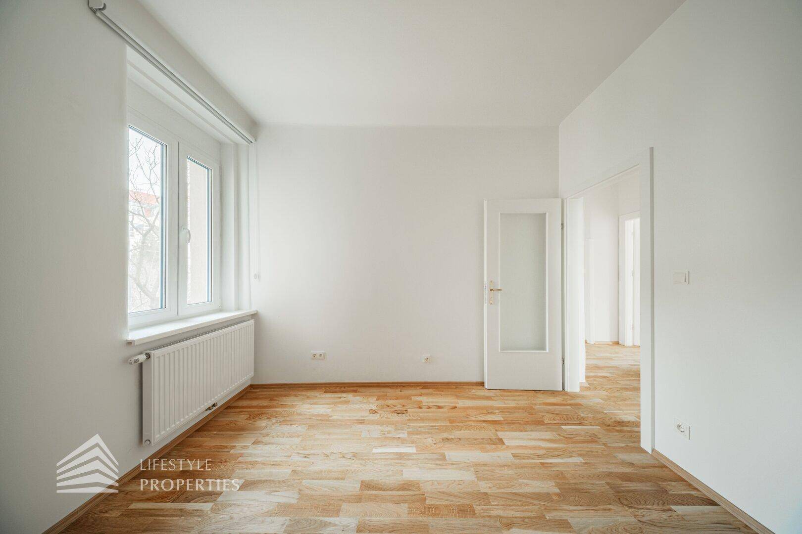 Helles Zimmer mit Parkettboden und einem großen Fenster, ideal als Schlaf- oder Arbeitszimmer.