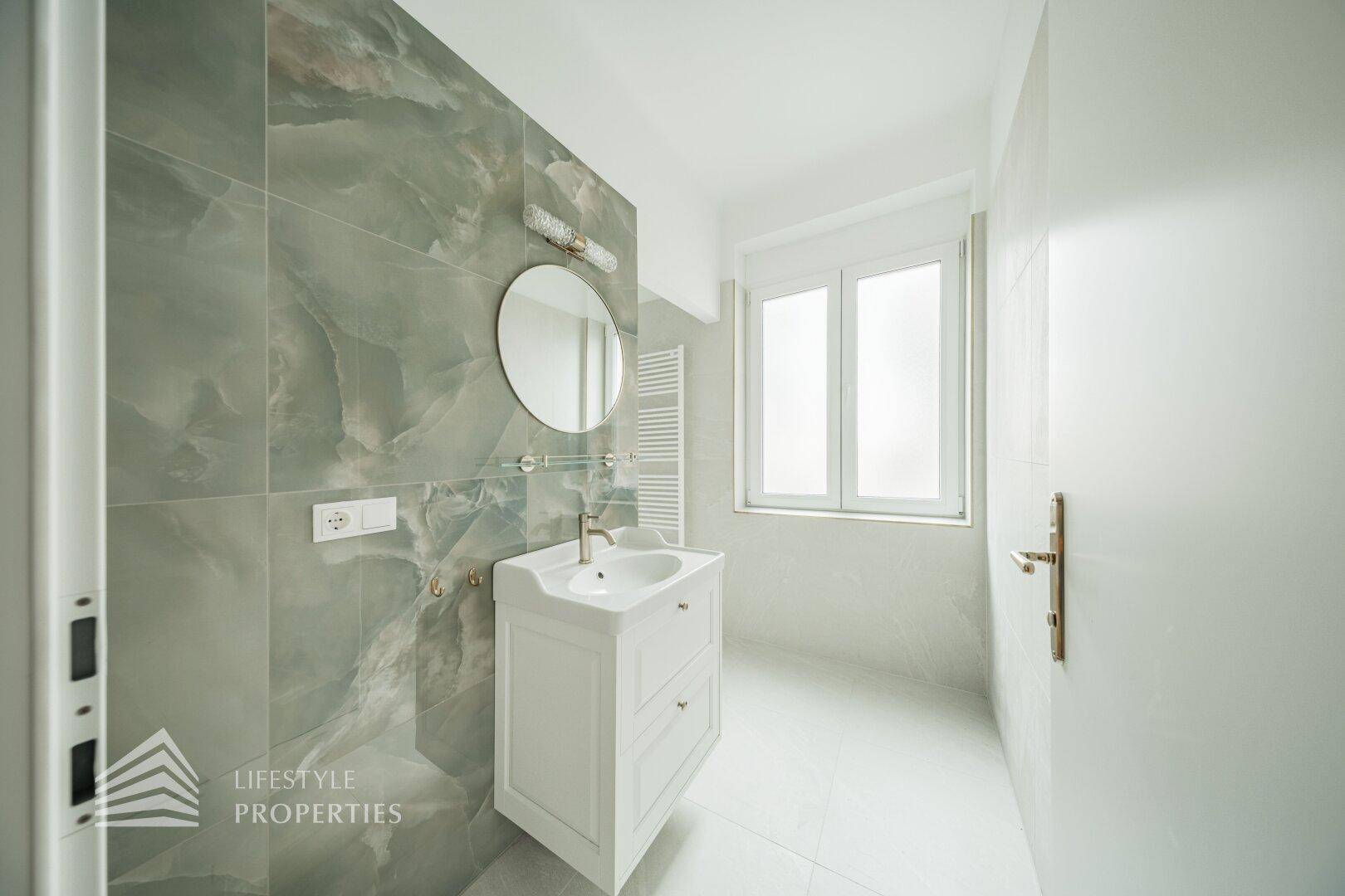 Modernes Badezimmer mit Waschtisch, Spiegel, beheiztem Handtuchhalter und Fenster.