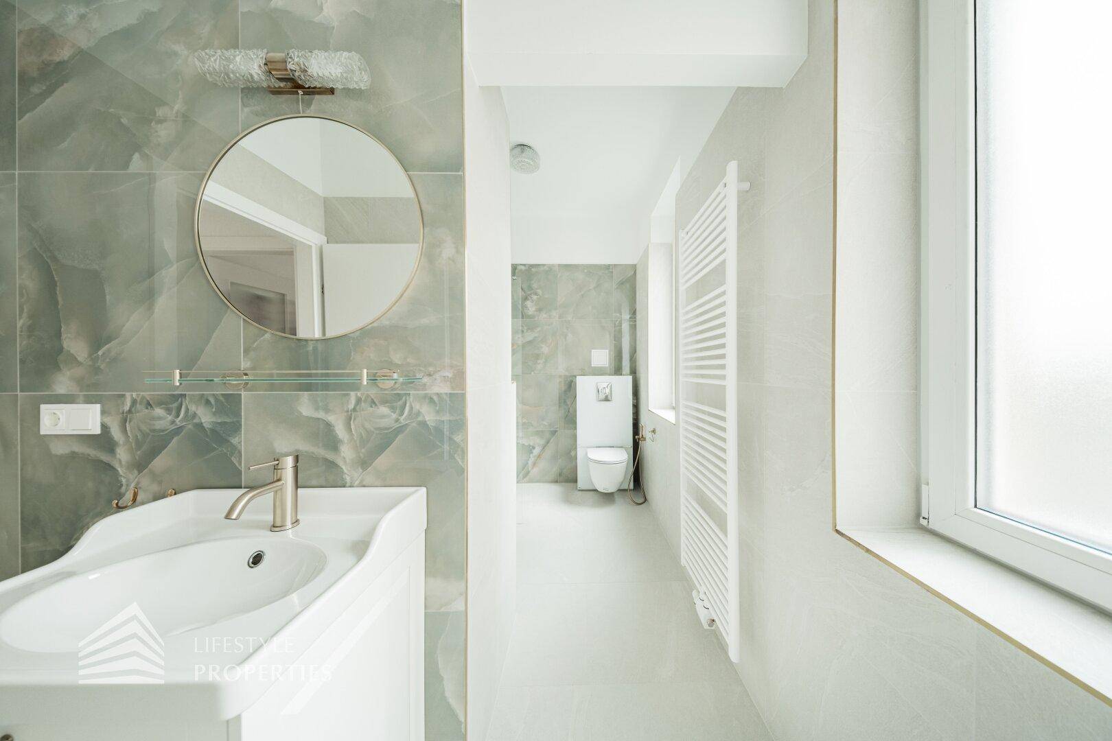 Elegantes Badezimmer mit Waschtisch, WC, beheiztem Handtuchhalter und modernen Fliesen.