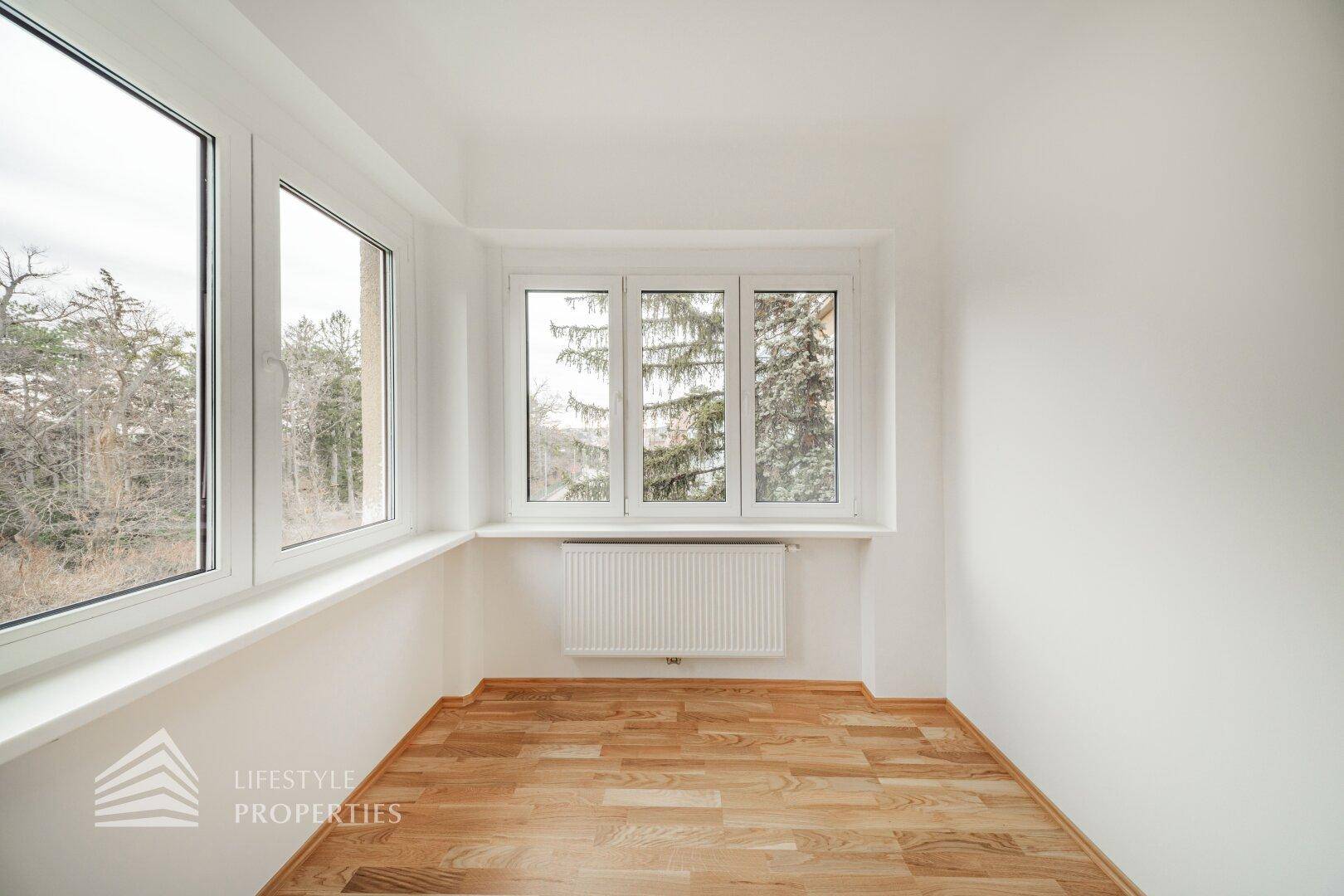 Heller Raum mit Parkettboden und großen Fenstern, die viel Tageslicht hereinlassen.