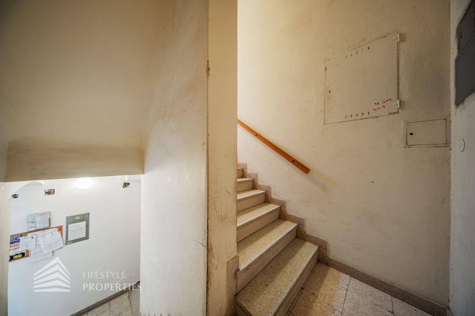 Treppenhaus mit Terrazzostufen und einem Holzgeländer, das in die obere Etage führt.