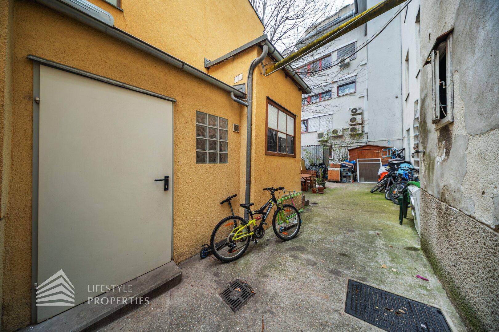 Hinterhof mit einer gelben Fassade, einem Nebengebäude und abgestellten Fahrrädern.