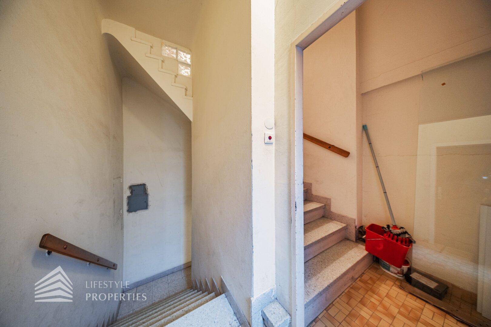Treppenhaus mit mehreren Etagen, Terrazzostufen und einem Fenster mit Glasbausteinen.