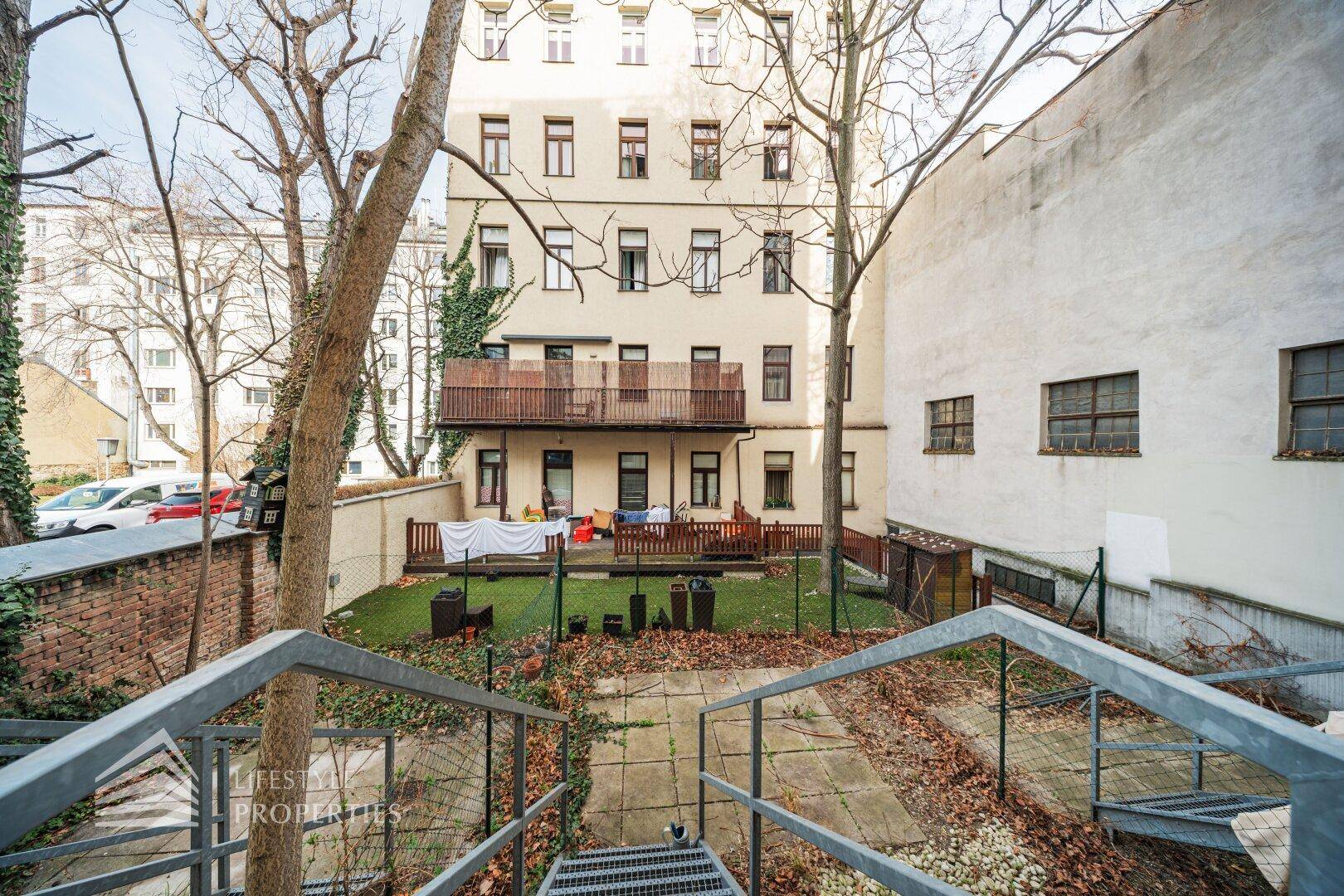 Hinterhof mit Gartenbereich, Treppenabgang und Blick auf die Gebäudefassade.