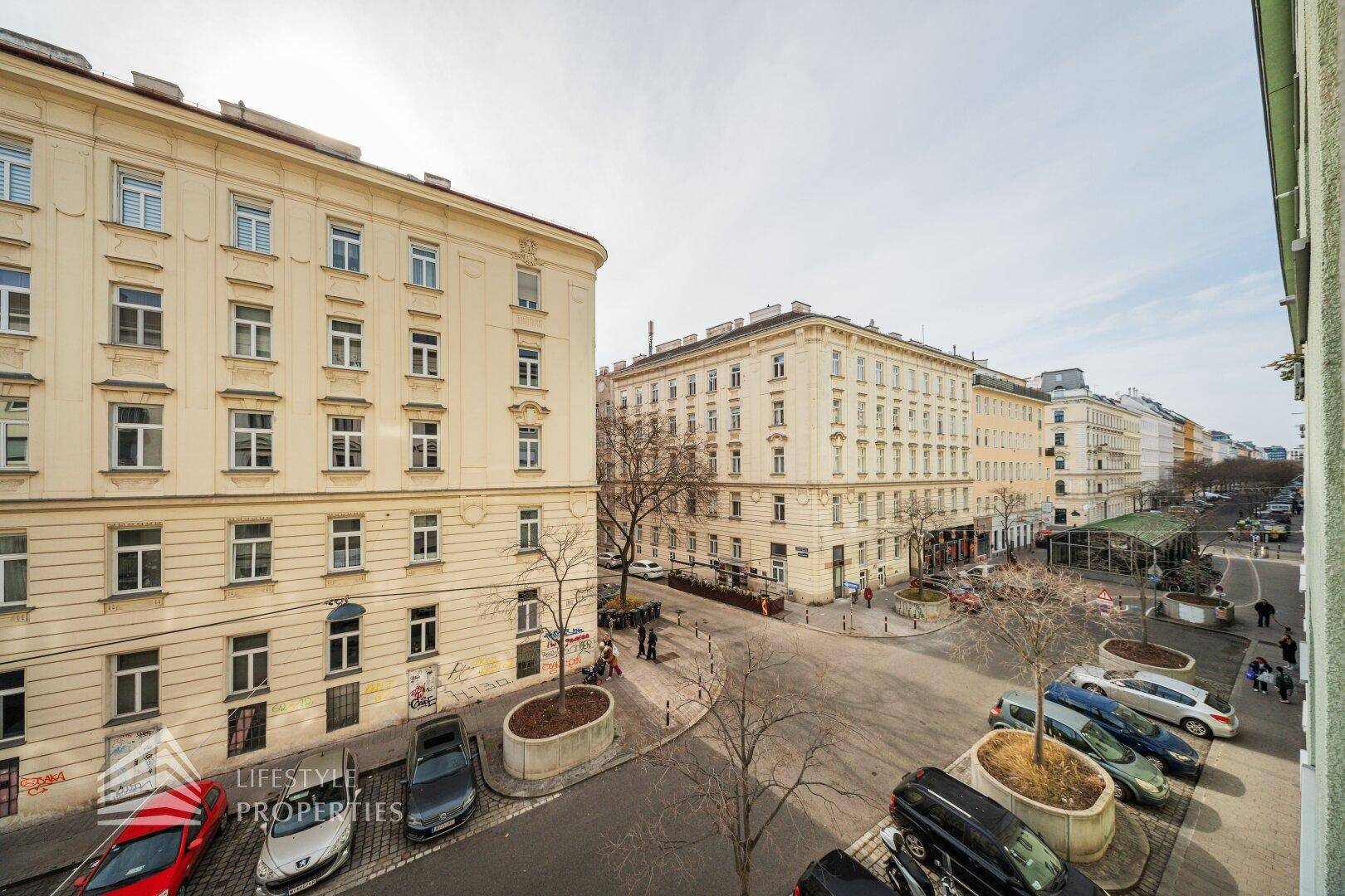 Blick über eine belebte Stadtstraße mit historischen Gebäuden und parkenden Autos.