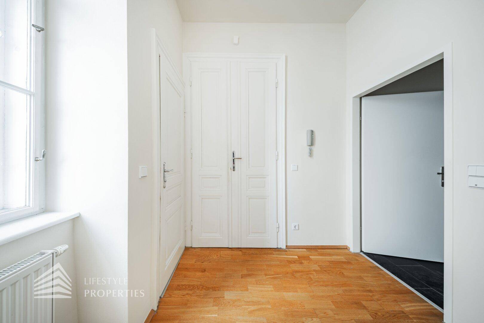 Heller Flur mit Parkettboden, weißen Türen und einem Fenster für Tageslicht.
