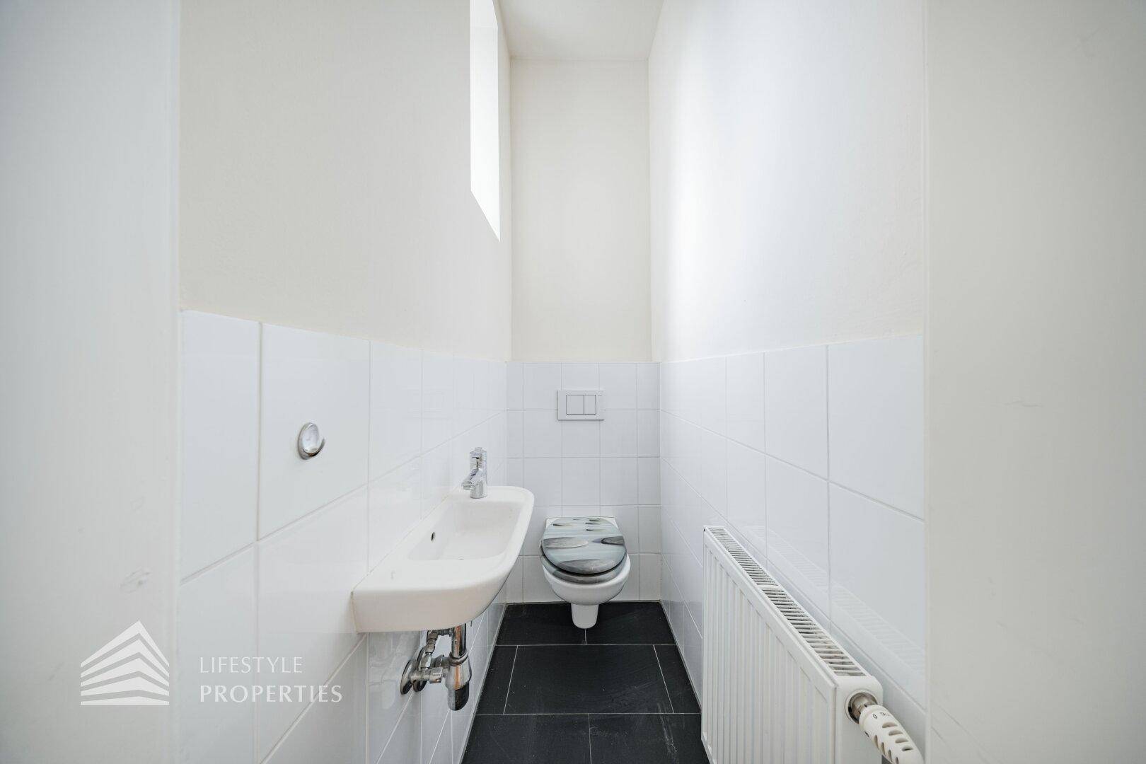 Modernes Gäste-WC mit weißen Fliesen, dunklem Boden und wandhängendem WC.