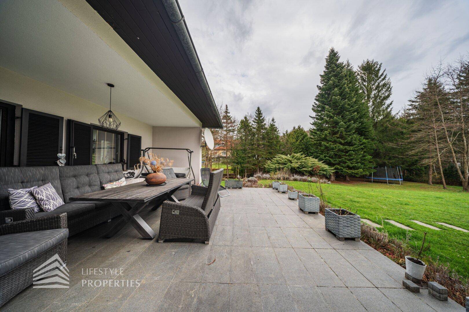 Geräumige Terrasse mit bequemen Outdoor-Möbeln und Blick auf den grünen Garten.