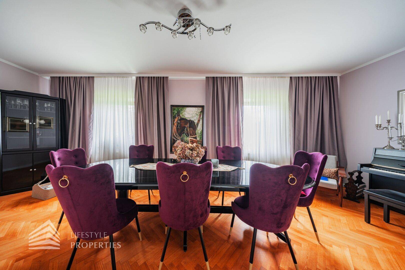 Elegantes Esszimmer mit großem schwarzen Tisch, Samtstühlen und Parkettboden.