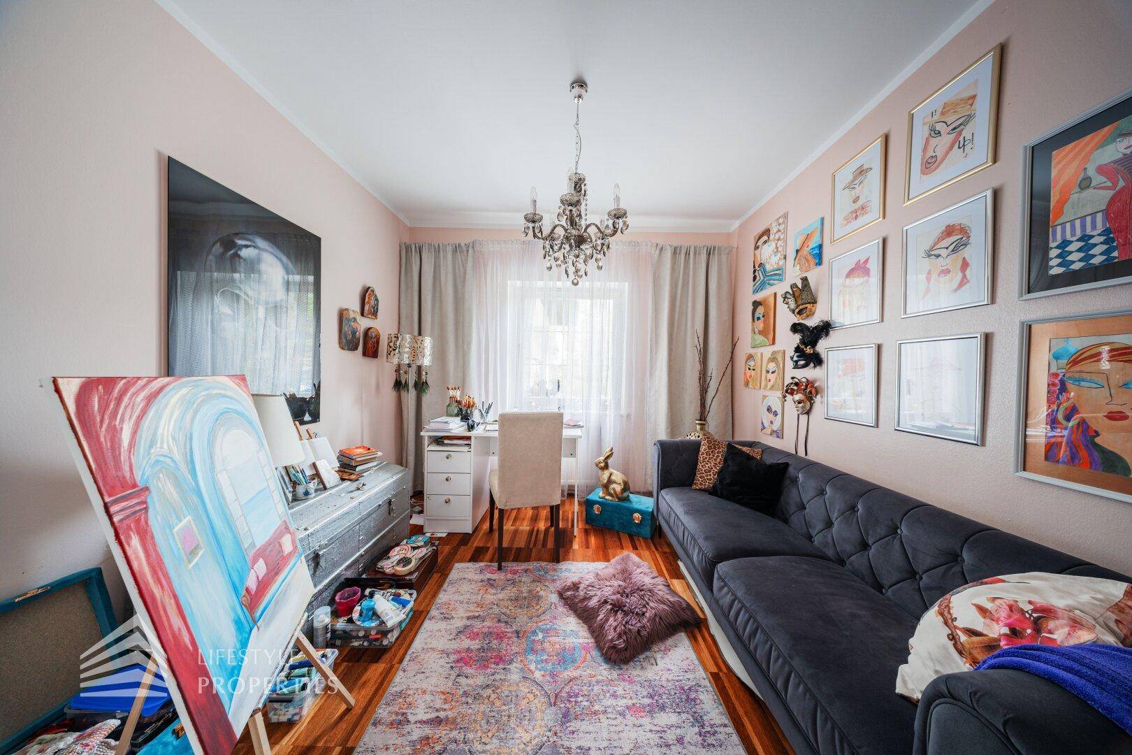 Kreativ gestaltetes Wohnzimmer mit Sofa, Schreibtisch und vielen Kunstwerken an den Wänden.