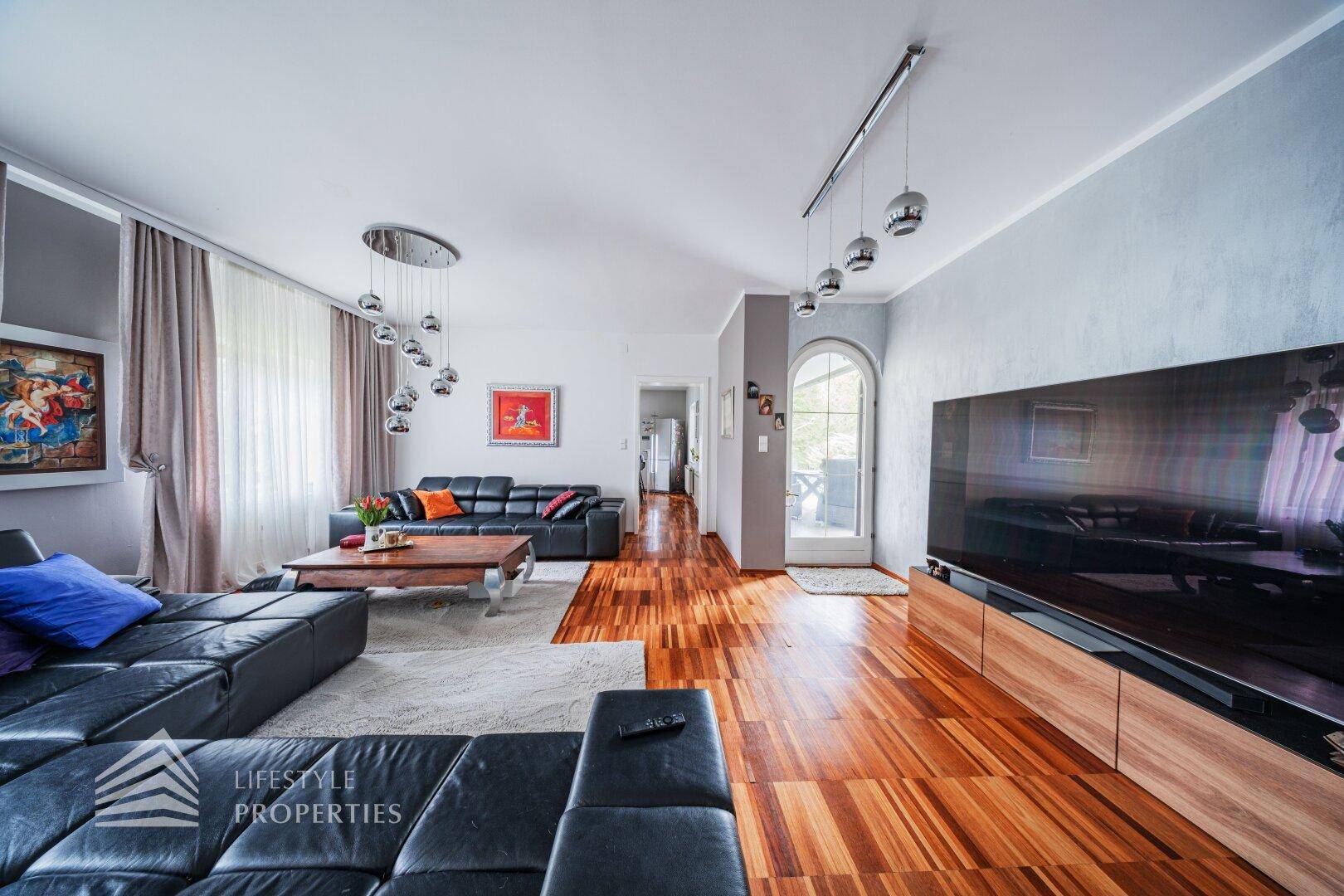 Geräumiges Wohnzimmer mit schwarzen Ledersofas, Holzboden und modernen Hängelampen.