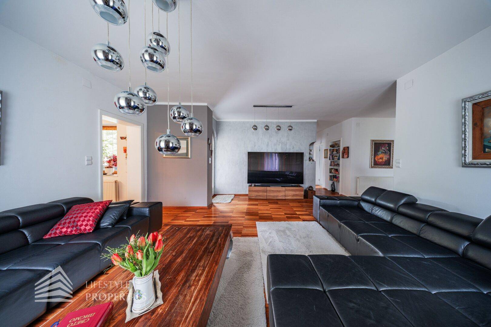Geräumiges Wohnzimmer mit dunklen Ledersofas, Holzboden und moderner Deckenbeleuchtung.