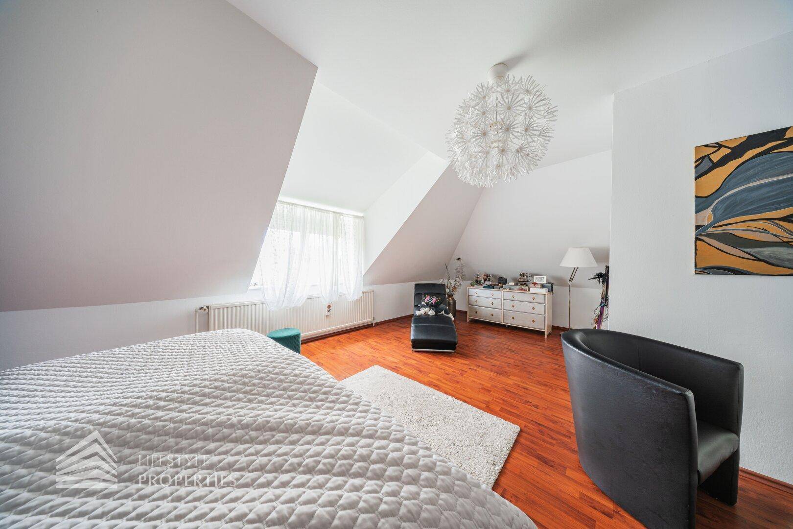 Geräumiges Schlafzimmer im Dachgeschoss mit Holzboden, Sitzgelegenheiten und dekorativer Beleuchtung.