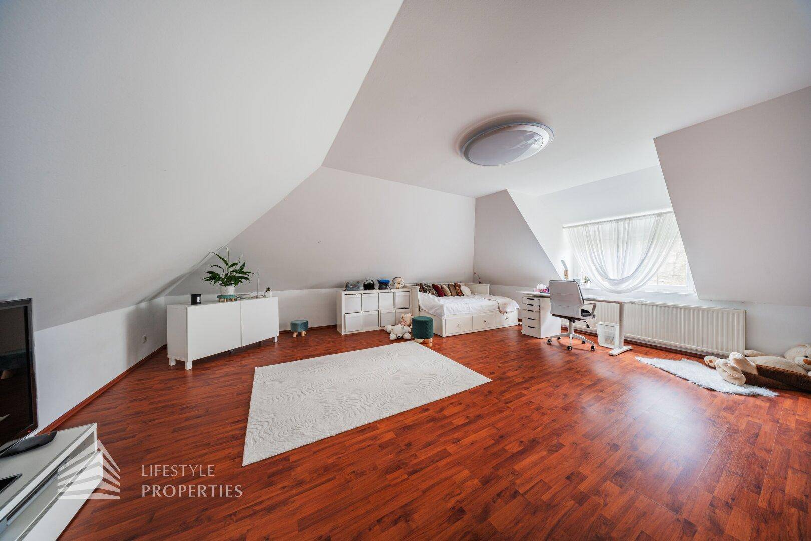 Kinderzimmer im Dachgeschoss mit Holzboden, Schreibtisch und viel Stauraum.