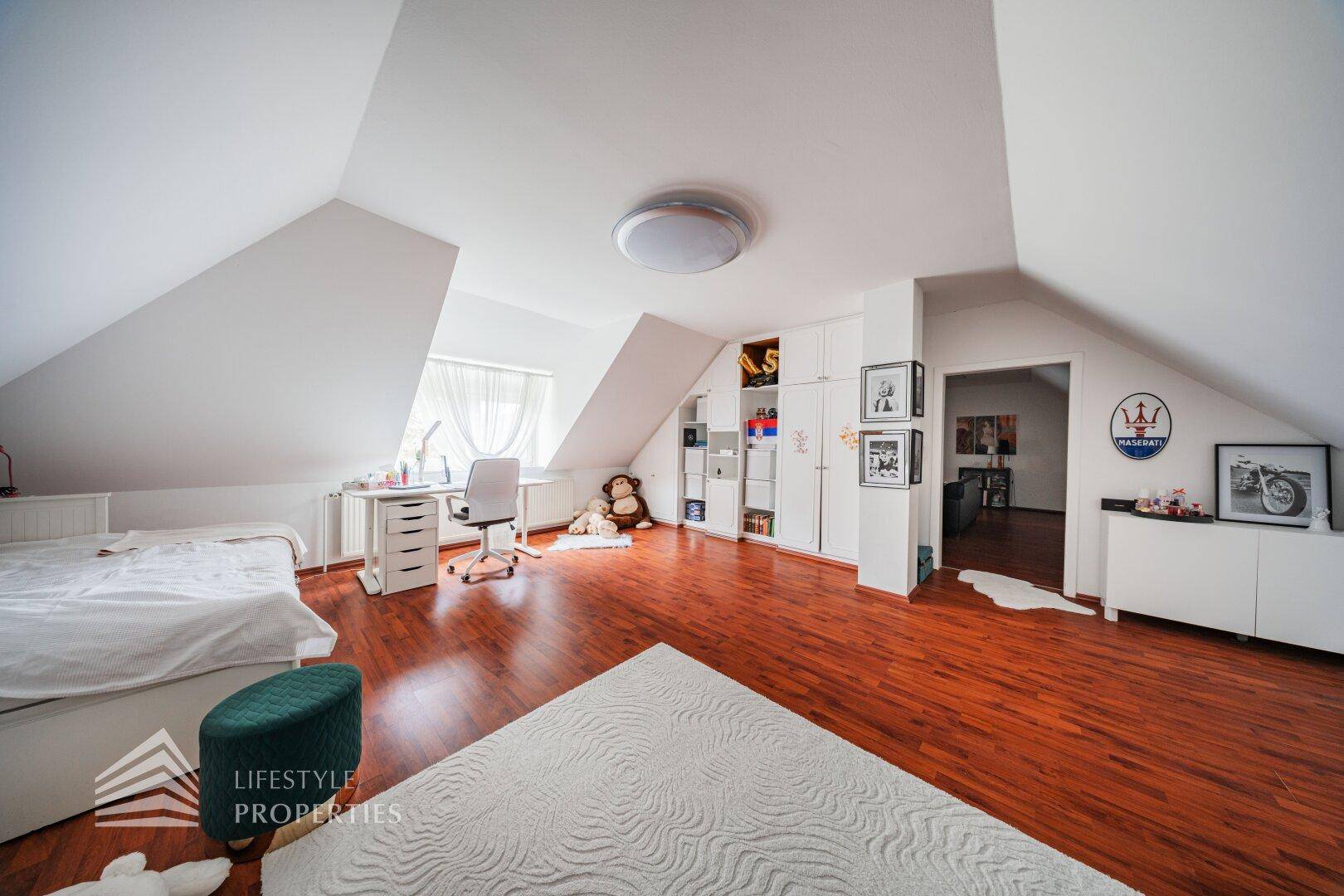 Helles Kinderzimmer im Dachgeschoss mit Holzboden, Schreibtisch und integrierten Regalen.