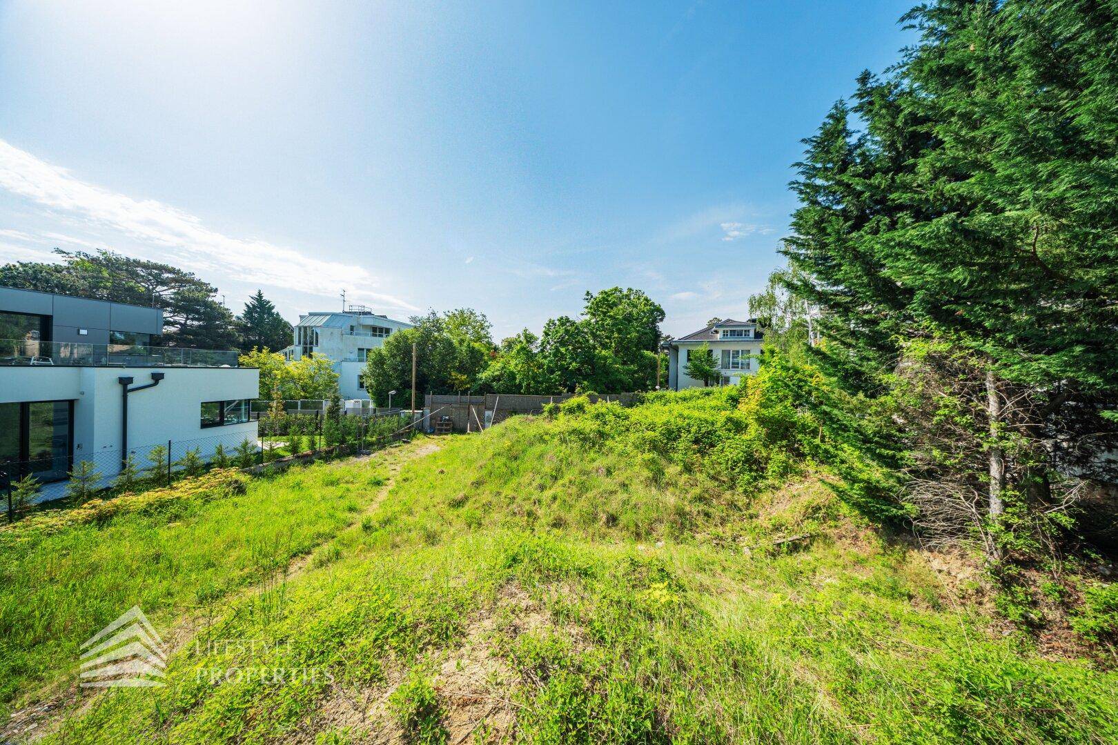 Sonniger Blick über ein grünes, hügeliges Grundstück mit modernen Häusern im Hintergrund.