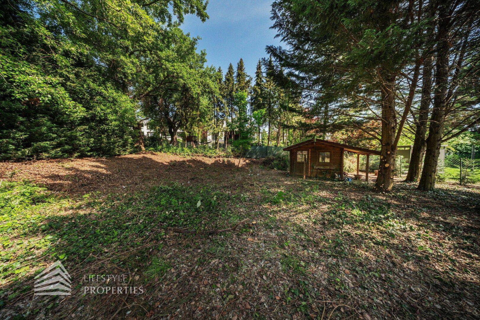 Weitläufiges Grundstück mit einem kleinen Gartenhaus und altem Baumbestand.