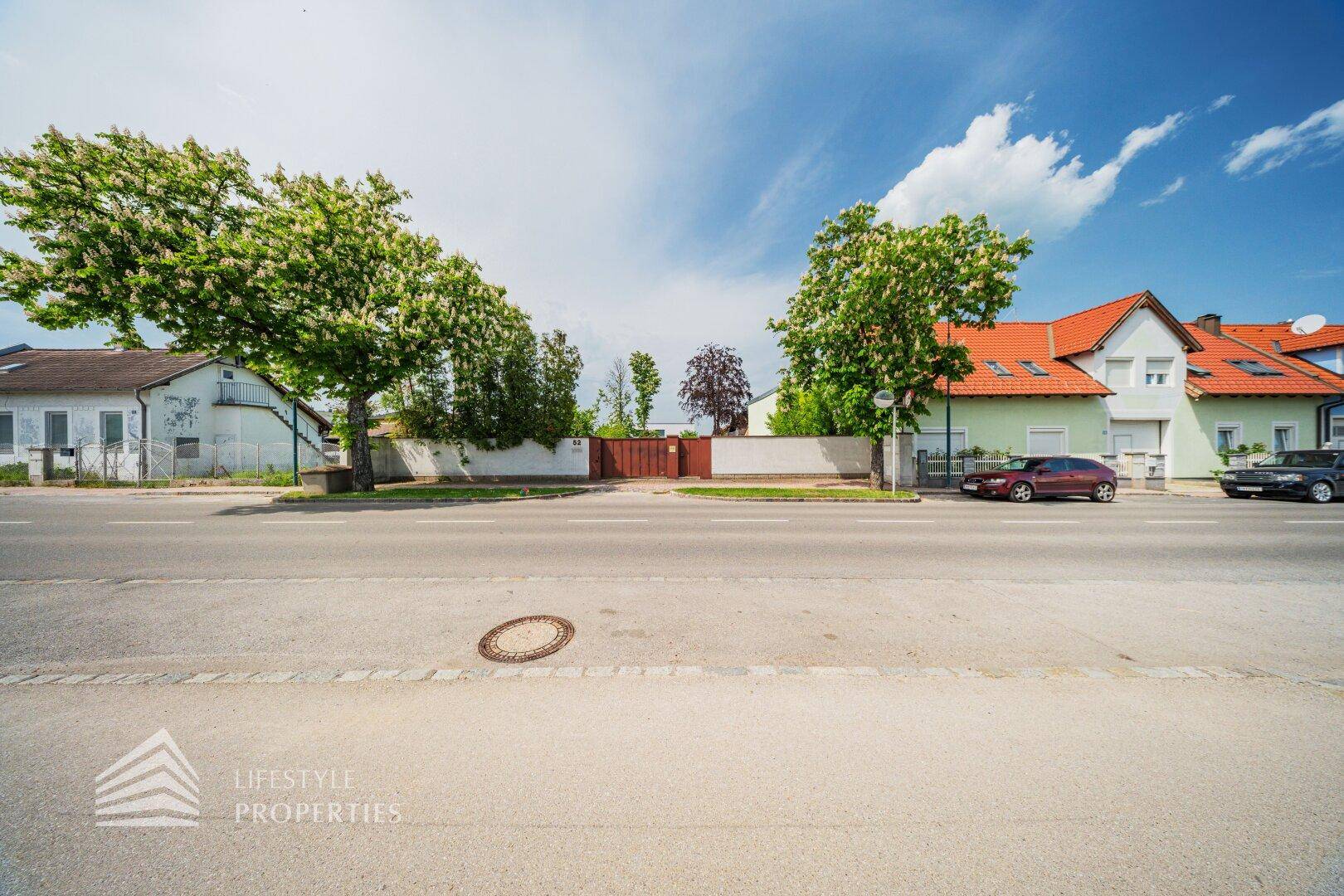 Straßenansicht des Anwesens mit Zaun, Tor und angrenzenden Häusern.