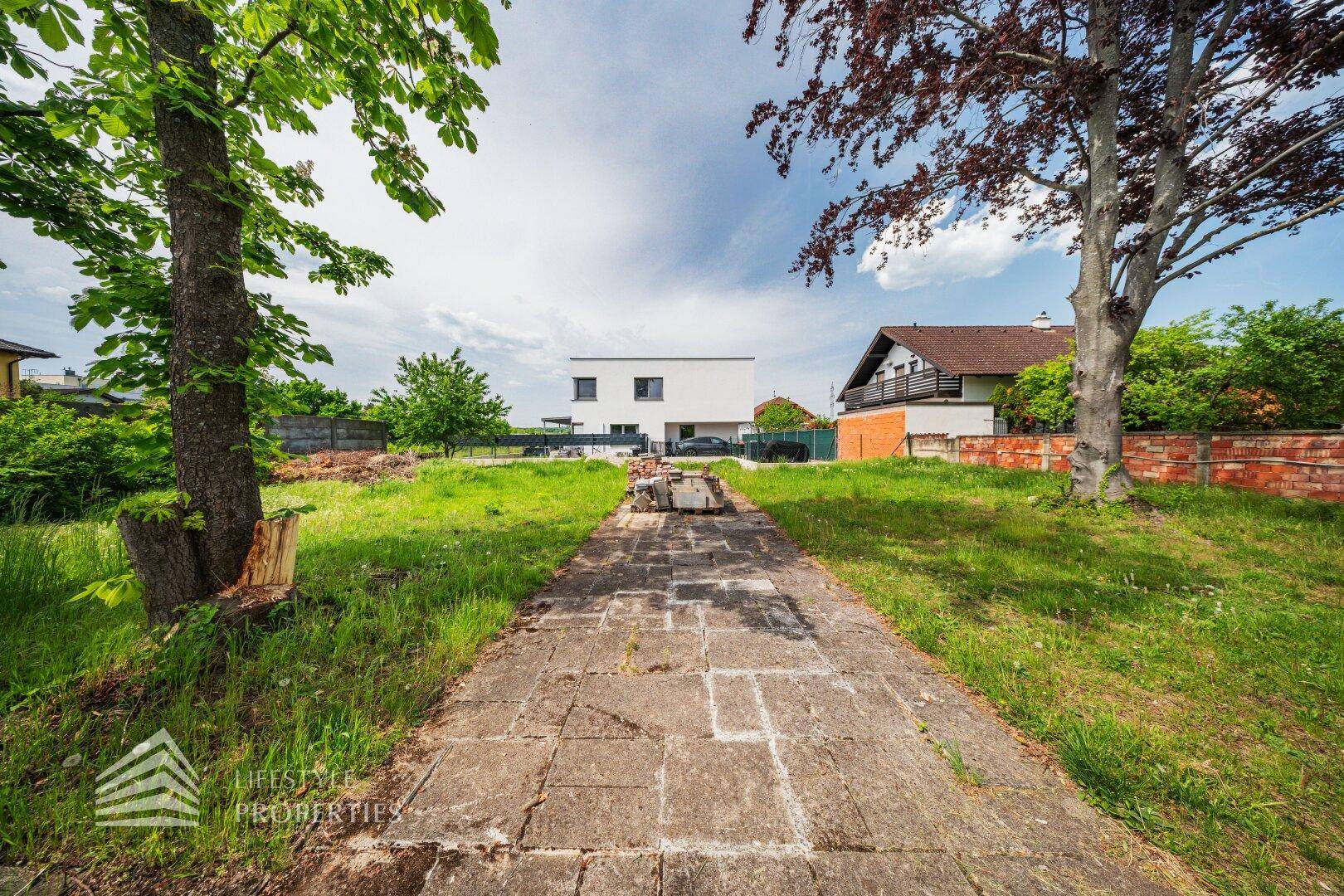 Gepflasterter Weg mit Grasstreifen, der auf ein modernes weißes Gebäude im Hintergrund zuläuft.