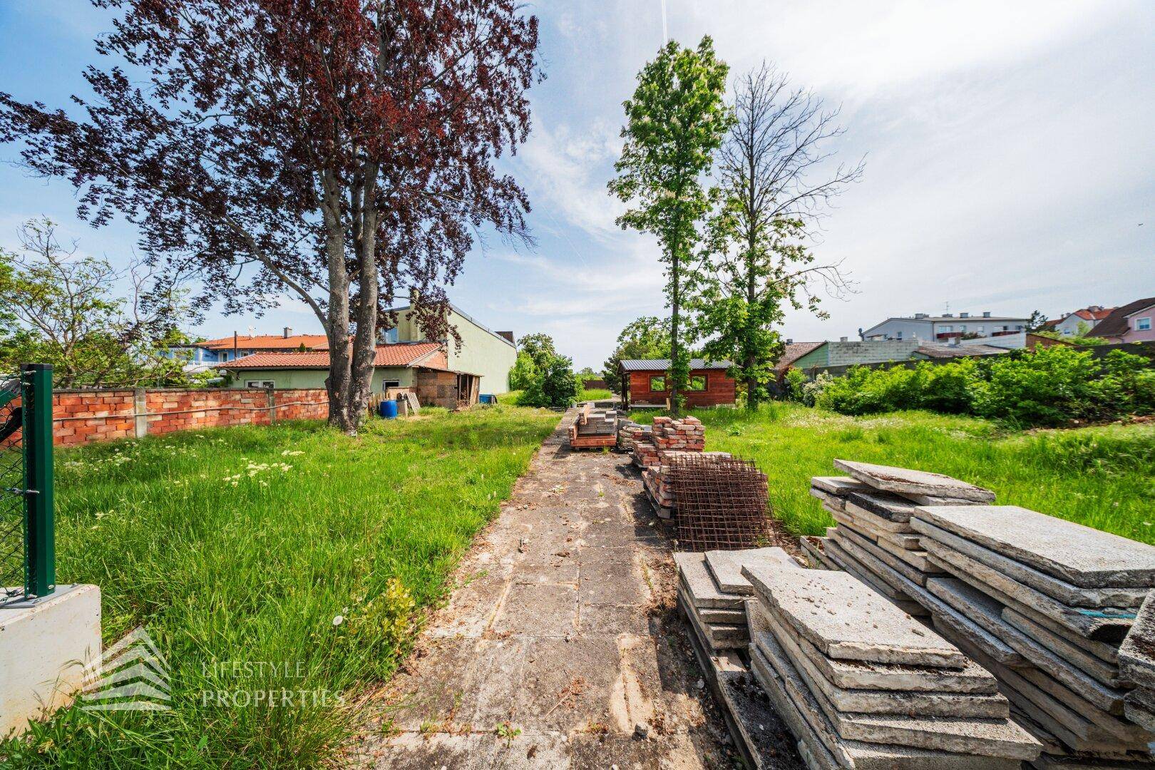 Gepflasterter Weg mit gestapelten Betonplatten und einem kleinen Schuppen im Hintergrund.