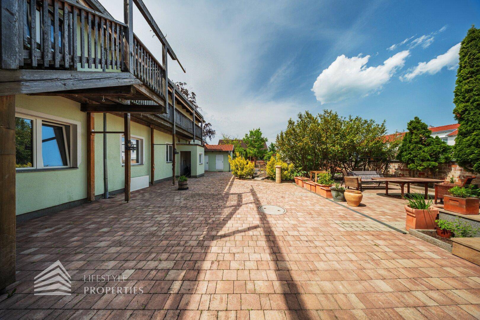Große gepflasterte Terrasse mit Gartenmöbeln und Topfpflanzen, ideal für Entspannung.