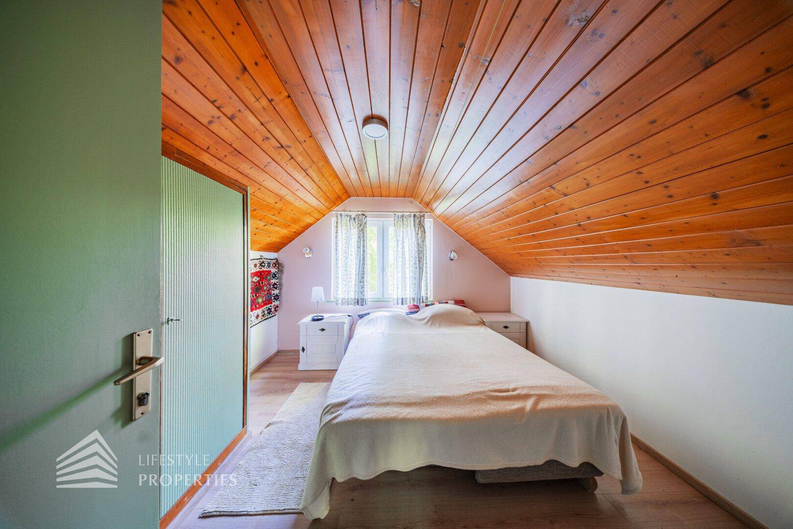 Gemütliches Schlafzimmer im Dachgeschoss mit sichtbarer Holzdecke und schrägen Wänden.