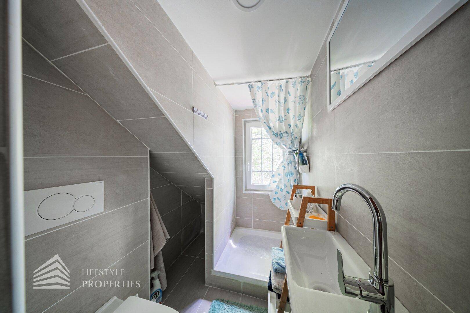 Modernes Badezimmer mit grauen Fliesen, Dusche und Dachschräge.