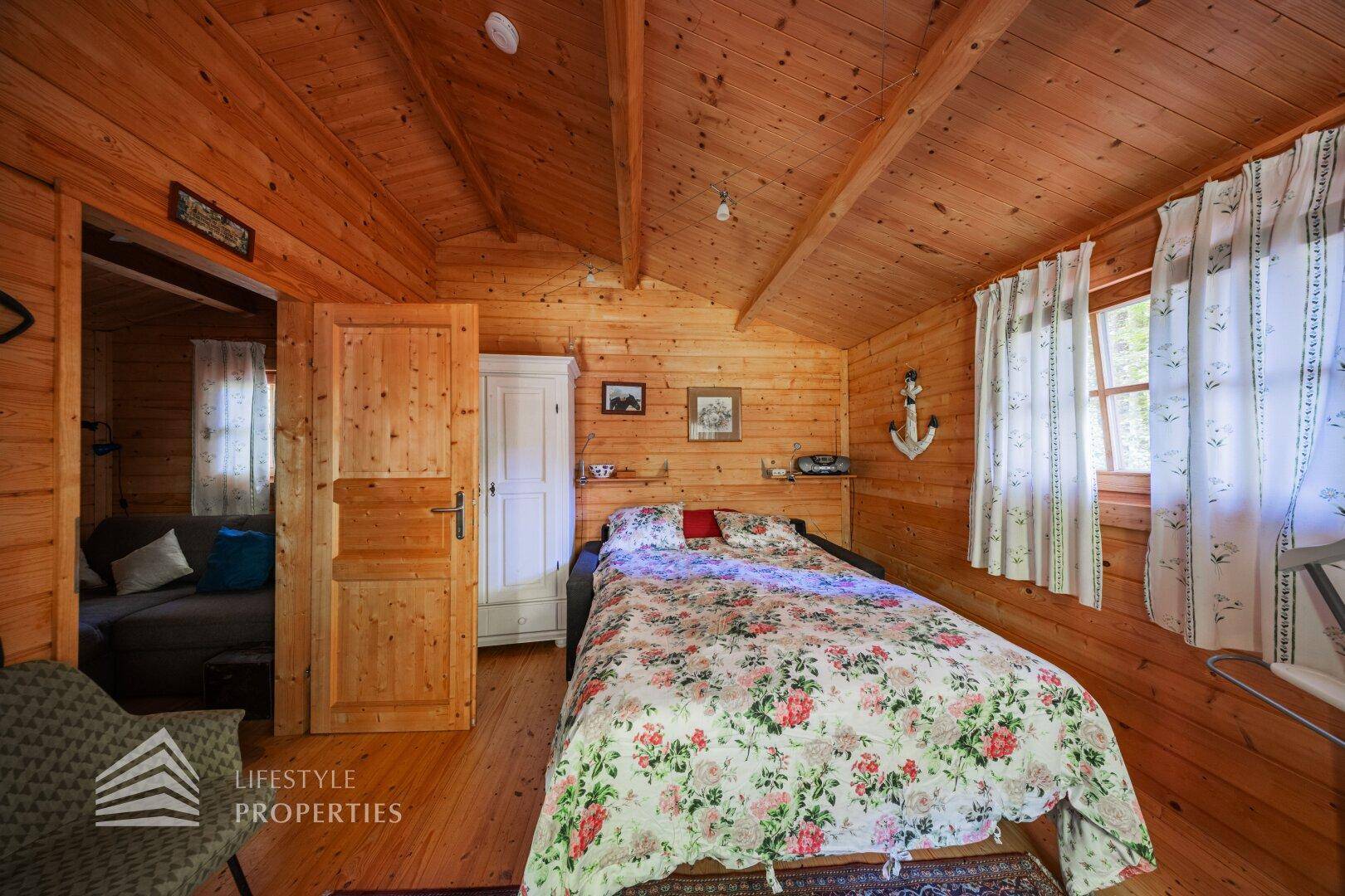 Gemütliches Schlafzimmer in einer Holzhütte mit floraler Bettwäsche und Dachschrägen.