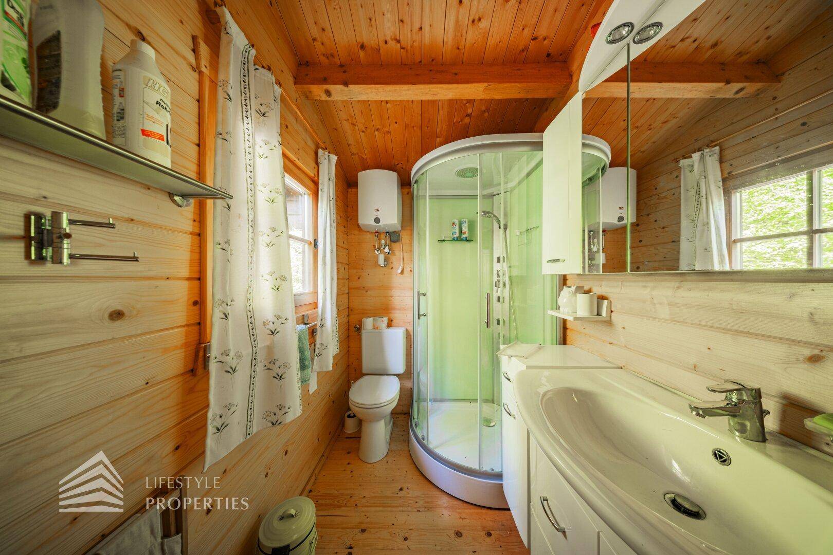Badezimmer in einer Holzhütte mit Duschkabine, Waschbecken und Holzvertäfelung.