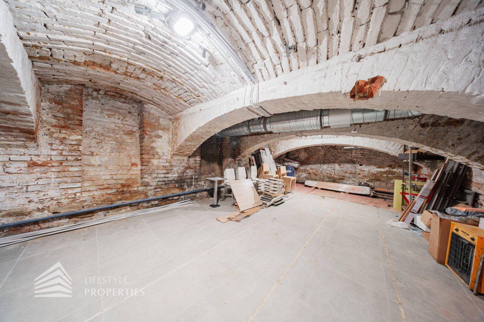 Historischer Kellerraum mit Gewölbedecken aus Ziegeln und Betonboden, derzeit als Lager genutzt.