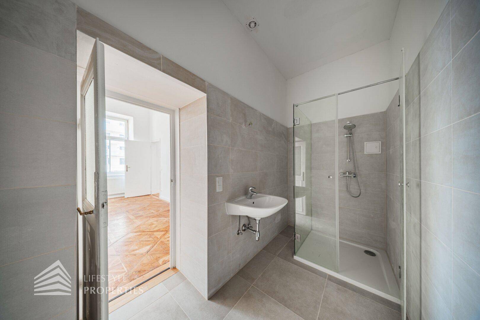 Modernes Badezimmer mit grauen Fliesen, einer ebenerdigen Dusche und einem Waschbecken.