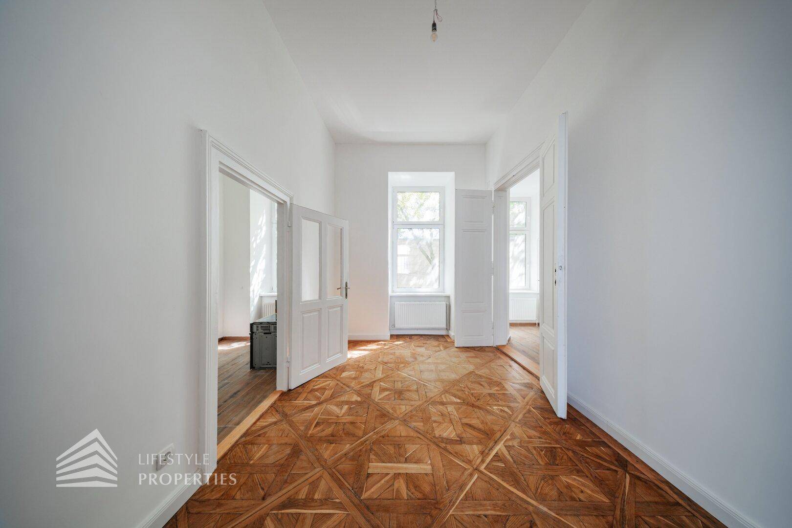 Heller Flur mit kunstvollem Parkettboden und hohen Türen, der verschiedene Zimmer verbindet.