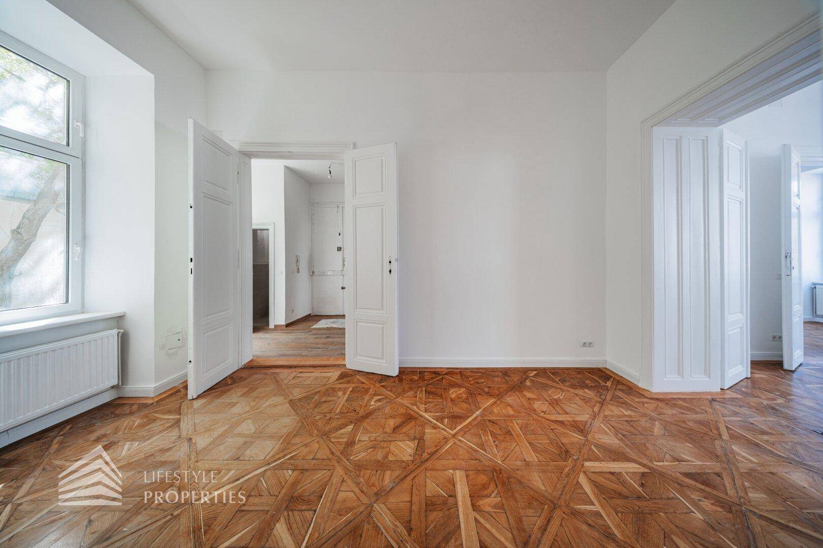 Geräumiges, leeres Zimmer mit kunstvollem Parkettboden und hohen Doppeltüren.