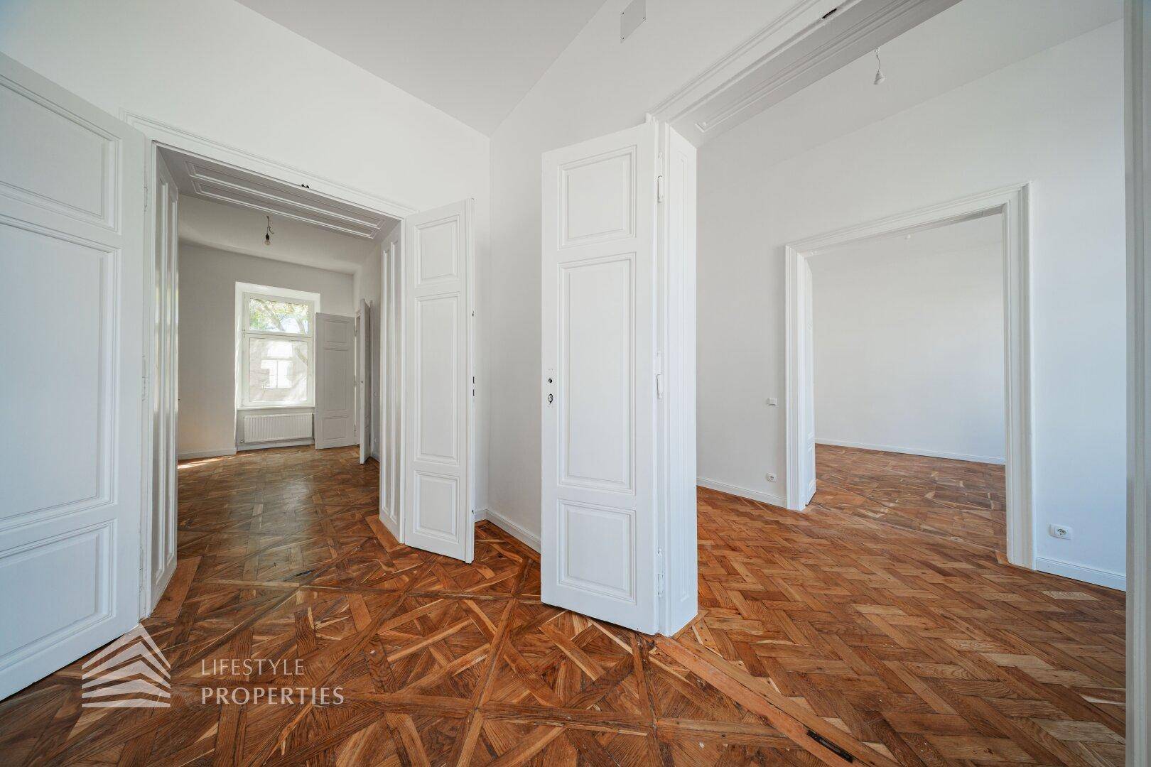 Heller Innenraum mit kunstvollem Parkettboden und hohen Türen, der mehrere Zimmer verbindet.