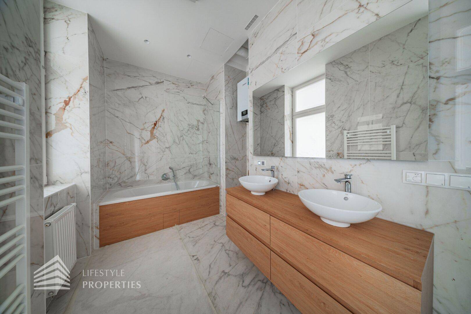 Modernes Badezimmer mit Marmorfliesen, Doppelwaschbecken, Badewanne und beheiztem Handtuchhalter.